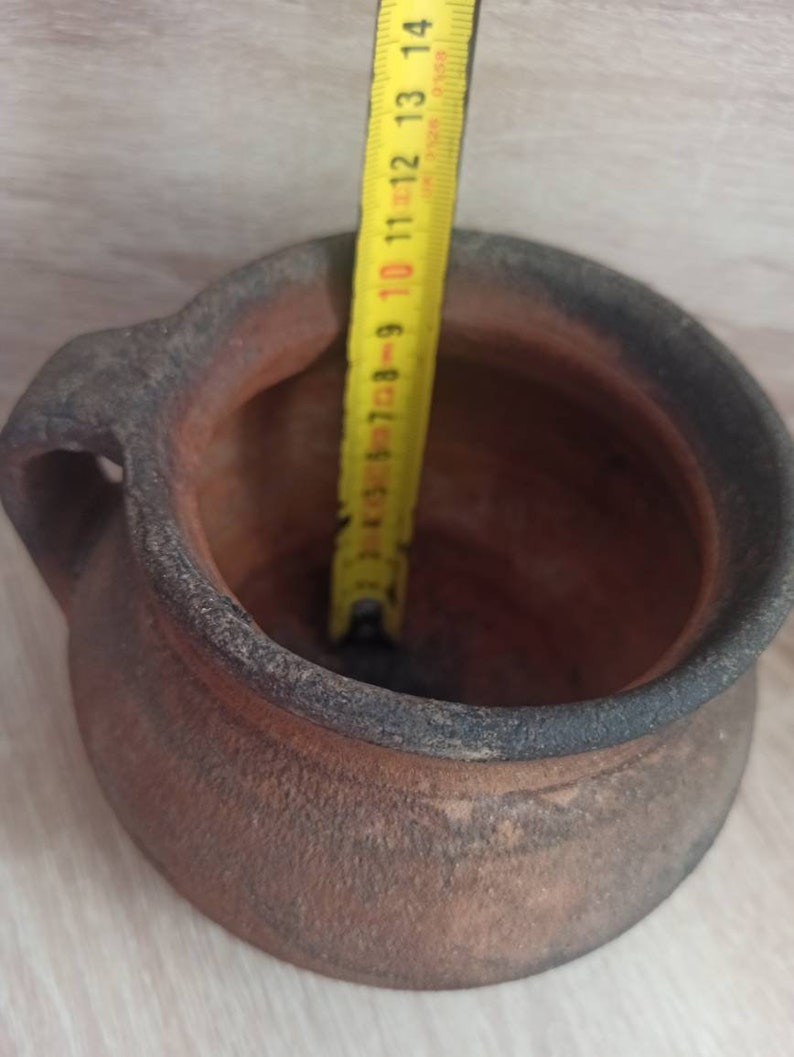 May include: A terracotta pot with a handle, measuring 14 inches in diameter. The pot is brown and has a rough texture.