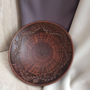 May include: A brown ceramic plate with a decorative design of leaves around the rim.