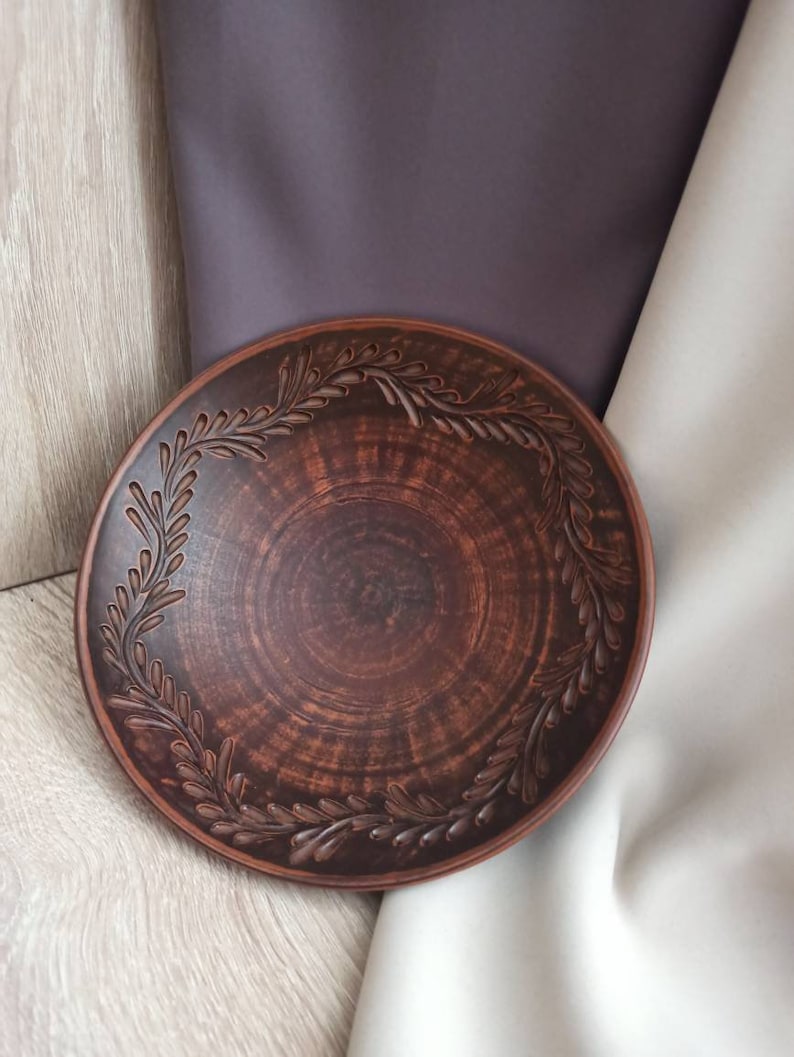 May include: A brown ceramic plate with a decorative design of leaves around the rim.