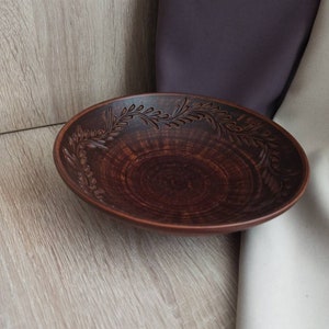 May include: A brown ceramic bowl with a decorative floral design around the rim. The bowl is handmade and has a rustic look.