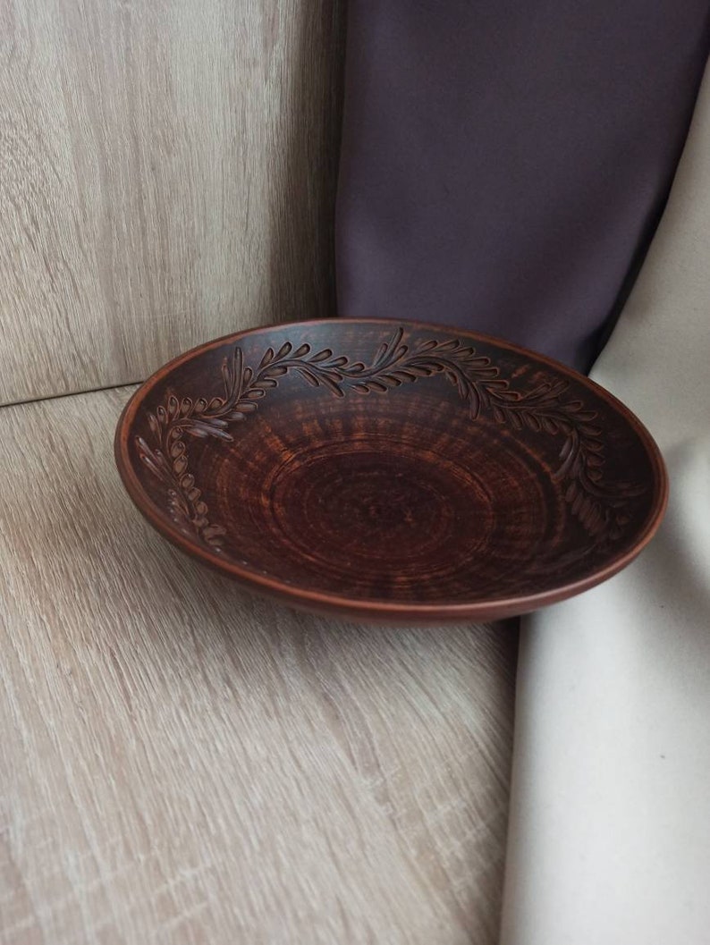 May include: A brown ceramic bowl with a decorative floral design around the rim. The bowl is handmade and has a rustic look.