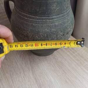 Pode incluir: Um jarro cinza escuro, de estilo antigo, com uma al&ccedil;a. O jarro tem aproximadamente 14 cm de di&acirc;metro. Apresenta uma superf&iacute;cie texturizada e uma forma arredondada cl&aacute;ssica, sugerindo que &eacute; vintage.