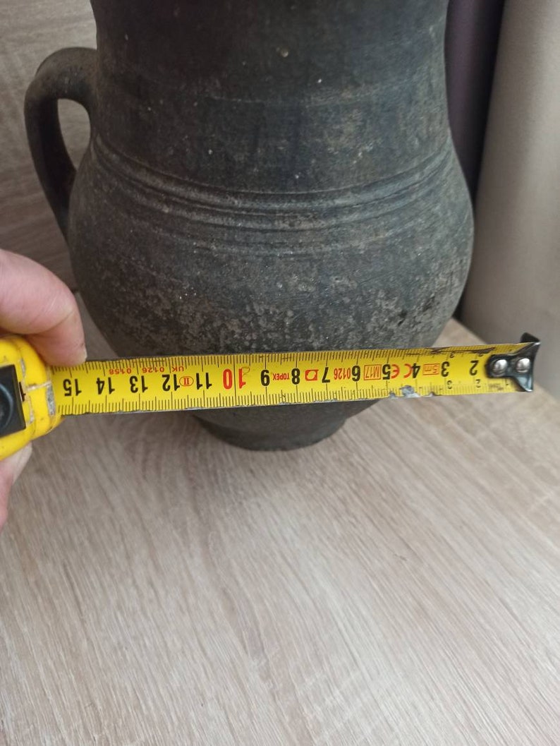 Pode incluir: Um jarro cinza escuro, de estilo antigo, com uma al&ccedil;a. O jarro tem aproximadamente 14 cm de di&acirc;metro. Apresenta uma superf&iacute;cie texturizada e uma forma arredondada cl&aacute;ssica, sugerindo que &eacute; vintage.