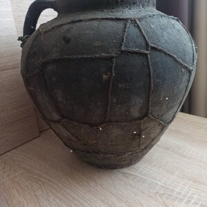 May include: A large, dark brown clay pot with a wide mouth and a handle. The pot is decorated with a pattern of woven strips.