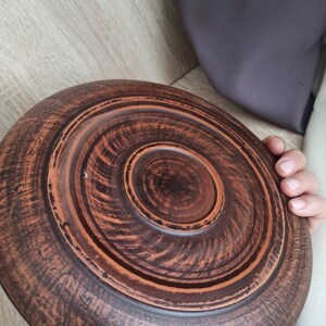 May include: A brown clay serving dish with a circular shape and a raised center. The dish has a rustic, handmade appearance.