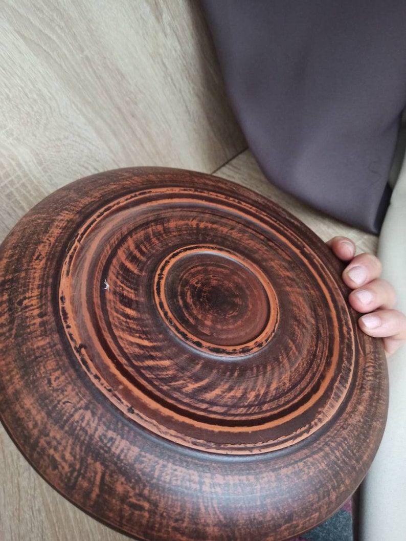 May include: A brown clay serving dish with a circular shape and a raised center. The dish has a rustic, handmade appearance.