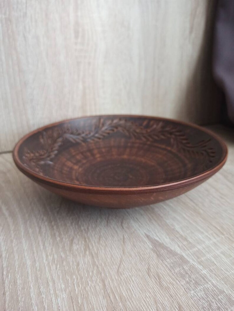 May include: A brown ceramic bowl with a decorative design of leaves around the rim. The bowl is slightly curved and has a smooth, glossy finish.