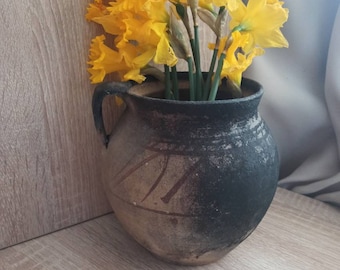 May include: A bunch of yellow daffodils in a rustic brown and black ceramic vase with a textured surface.