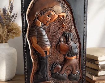 May include: A rectangular copper wall art piece featuring a relief design of a person in a cap and striped shirt interacting with a dog. The background has a textured, dotted pattern, and the entire scene is framed by a dark, studded border.