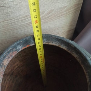 May include: A yellow measuring tape with black markings is placed inside a large, brown terracotta pot. The tape measures 35 inches.