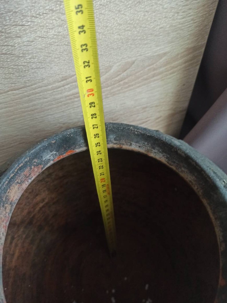 May include: A yellow measuring tape with black markings is placed inside a large, brown terracotta pot. The tape measures 35 inches.