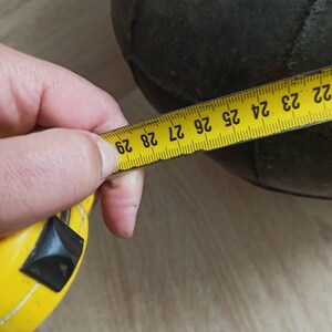 K&ouml;nnte beinhalten: Ein dunkelgr&uuml;ner, runder Gegenstand wird mit einem gelben Ma&szlig;band gemessen. Das Ma&szlig;band zeigt eine Messung von etwa 74 cm an. Der Gegenstand scheint aus einem strukturierten Material zu bestehen.