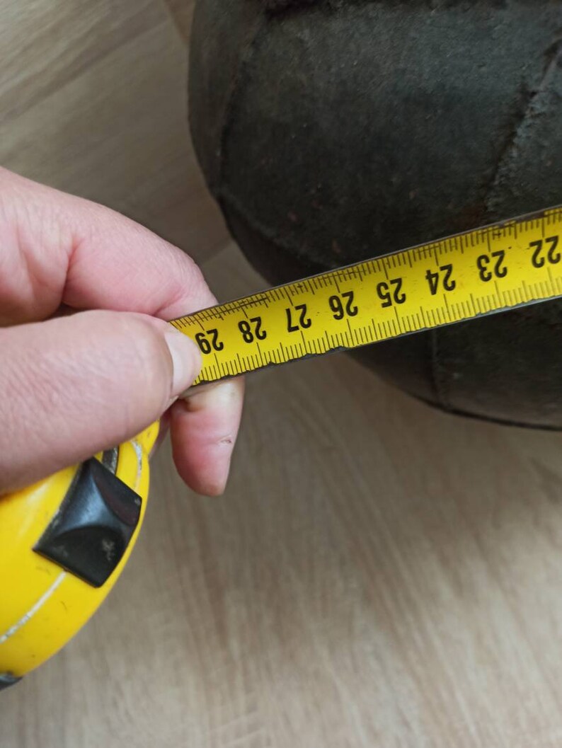 K&ouml;nnte beinhalten: Ein dunkelgr&uuml;ner, runder Gegenstand wird mit einem gelben Ma&szlig;band gemessen. Das Ma&szlig;band zeigt eine Messung von etwa 74 cm an. Der Gegenstand scheint aus einem strukturierten Material zu bestehen.