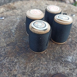 May include: Four spools of black thread with wooden tops. The spools have labels with text that is partially visible.