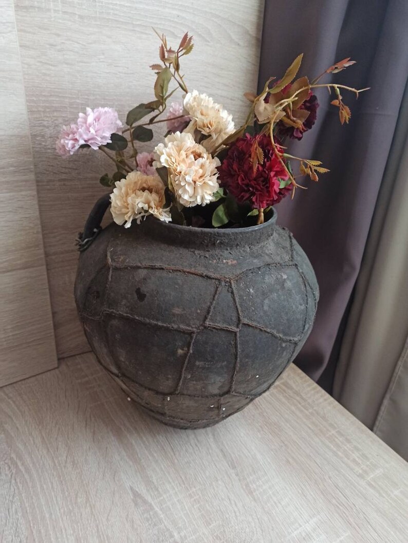 May include: A dark brown ceramic vase with a woven pattern, filled with a bouquet of pink, white, and red flowers.