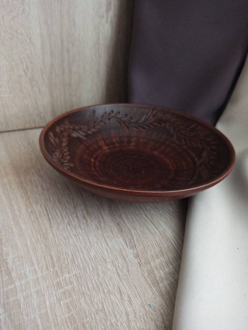 May include: A brown ceramic bowl with a decorative floral design. The bowl is empty and sitting on a light wood surface.