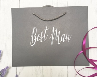 May include: A gray gift bag with a white rope handle and the text "Best Man" printed in white on the front.