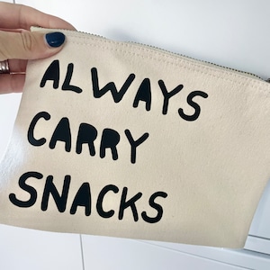 May include: A beige canvas zippered pouch with black text that reads "ALWAYS CARRY SNACKS".