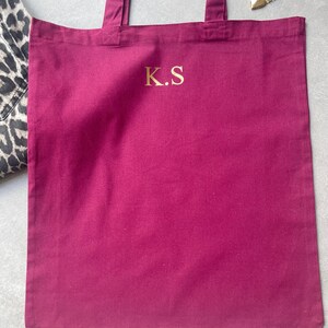 Puede incluir: Una bolsa de tela de color burdeos con un monograma bordado en oro "K.S."