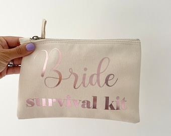 May include: A beige canvas zippered pouch with the text "Bride survival kit" in pink foil lettering.