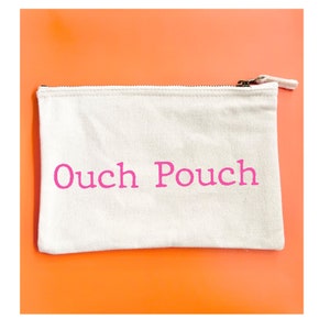 May include: A white canvas zippered pouch with the words "Ouch Pouch" printed in pink.