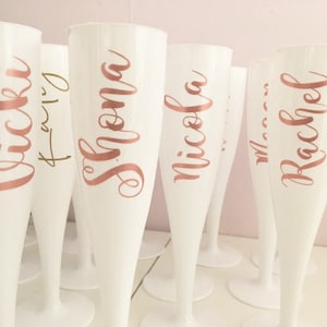 Puede incluir: Conjunto de copas de champán de plástico blanco con letras doradas rosas. Las copas están personalizadas con los nombres "Nicola", "Shona", "Emily", "Rachel" y "Vicki".