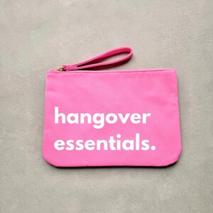 May include: A bright pink zippered pouch with a white handle and the text "hangover essentials." printed in white.
