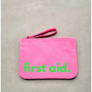 May include: A bright pink pouch with a zipper closure and a black handle. The pouch has the words "first aid" printed in neon green.