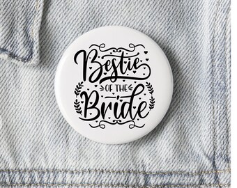 May include: White button with black text that reads "Bestie of the Bride" with small hearts and floral accents.