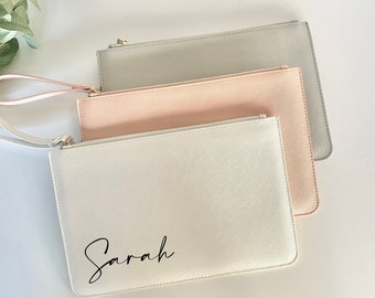 May include: Three zippered pouches in different colors: gray, pink, and white. The white pouch has the name "Sarah" written in black cursive.