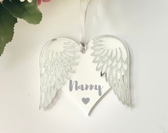 May include: White heart-shaped ornament with silver angel wings and the word "Nanny" written on it.