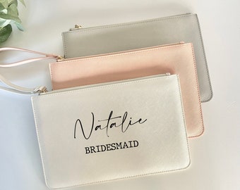 May include: Three zippered pouches in different colors: gray, pink, and white. The white pouch has the name "Natalie" and the word "BRIDESMAID" printed on it.