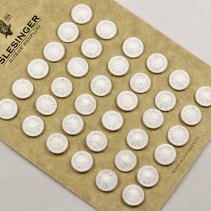 Op de afbeelding: Een vel met witte, met stof beklede knopen op een bruine papieren achtergrond. De knopen zijn in rijen gerangschikt en hebben een stervormig ontwerp. Het papier heeft de tekst "SLESINGER NITE'NE KNOFLIKY 1924" en "WWW.SLESINGER.CZ".