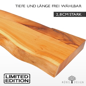 Può includere: Un ripiano in legno naturale con un bordo vivo, spesso 2,8 cm. Il ripiano è in legno marrone chiaro con una venatura naturale. Il testo "Limited Edition" è stampato su un rettangolo nero nell'angolo inferiore sinistro dell'immagine. Il testo "Tiefe und Länge frei wählbar 2,8cm stark" è stampato in nero nella parte superiore dell'immagine. Il testo "Möbel Design" è stampato in nero nell'angolo inferiore destro dell'immagine.