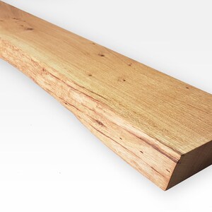 May include: A long, rustic wooden shelf with a natural, light brown finish. The shelf has a live edge on one side, giving it a unique and organic look.