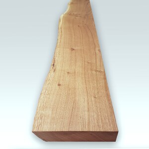 May include: A long, narrow piece of wood with a natural, light brown finish. The wood has a live edge on one side and a smooth, straight edge on the other. The wood is perfect for crafting projects or adding a rustic touch to your home decor.