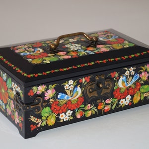 Può includere: Scatola di legno nera con coperchio a cerniera, ornata con vivaci motivi floreali e di uccelli in rosso, blu, giallo e verde. La scatola presenta una maniglia e chiusure in ottone, in stile arte popolare.