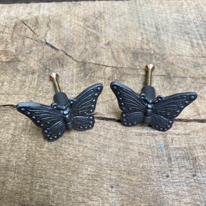 May include: Two black metal butterfly drawer pulls with a detailed design. The pulls have a screw on the back for attaching to a drawer.