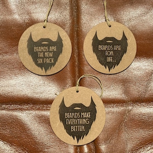 May include: Three round, brown, cardboard ornaments with black beard silhouettes and text. The text on the ornaments reads "Beards are the new six pack", "Beards are for life", and "Beards make everything better".