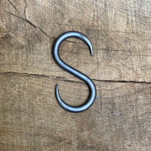May include: A silver metal S-shaped hook. The hook is on a wooden surface.