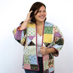 May include: A patchwork jacket with a variety of floral and geometric patterns in shades of purple, yellow, green, and blue. The jacket has a pink trim and a relaxed fit.