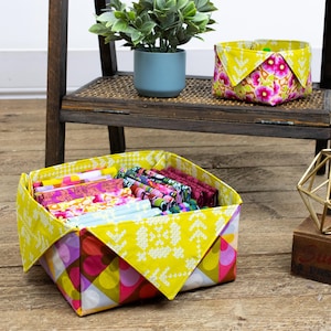May include: A yellow fabric storage bin with a geometric pattern and a white floral design. The bin is filled with colourful fabric scraps.