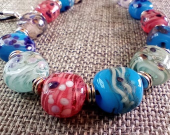 Handmade Lampwork Glass Bead Necklace in Shades of Blue, Rose and Clear with Added Opaque White and Frit on Leather Cord with Silver Spacers