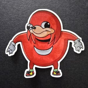 May include: A sticker depicting a cartoon character with a red body, a tan face, and black eyes. The character has a white outline, grey hands, and is wearing green, yellow, and red shoes. The character is smiling with its arms outstretched.
