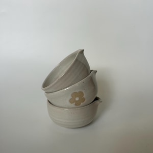 May include: Three stacked ceramic bowls with a light gray glaze. The middle bowl has a brown flower design.