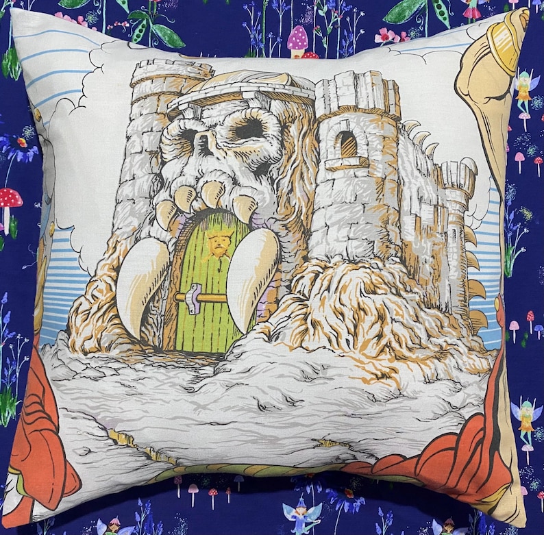 May include: Square decorative pillow featuring a detailed illustration of a castle with a skull-shaped entrance, a green door, and tall towers. The pillow has a white background with a blue and orange border.