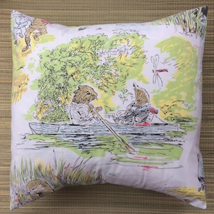 Puede incluir: Una funda de almohada blanca con una ilustración caprichosa de dos animales en un bote en un lago. Los animales están rodeados de árboles verdes y juncos. Una libélula vuela sobre el bote.