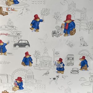 May include: A white wallpaper featuring a repeating pattern of Paddington Bear in various poses. Paddington is wearing a red hat and blue coat. The background features grey outlines of London landmarks, including Big Ben, the London Eye, and a double-decker bus.