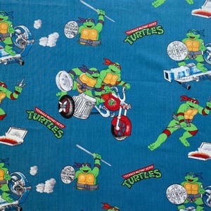 May include: A blue fabric with a repeating pattern of Teenage Mutant Ninja Turtles characters. The turtles are wearing red bandanas and are in various poses. The fabric also features the words "Teenage Mutant Hero Turtles" and "City Sewer" in a white font.