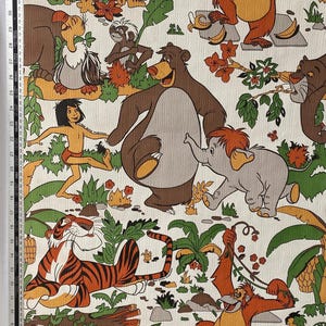 Op de afbeelding: Een witte stof met een herhalend patroon van jungledieren, waaronder een tijger, een beer, een aap en een olifant. De dieren zijn in cartoon-stijl afgebeeld en worden omringd door groene bladeren en bloemen.